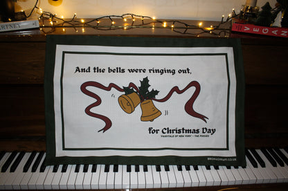 Irish Christmas tea towel with traditional festive illustrations of bells, holly, and ribbons, captioned with lyrics from a iconic Pogues song