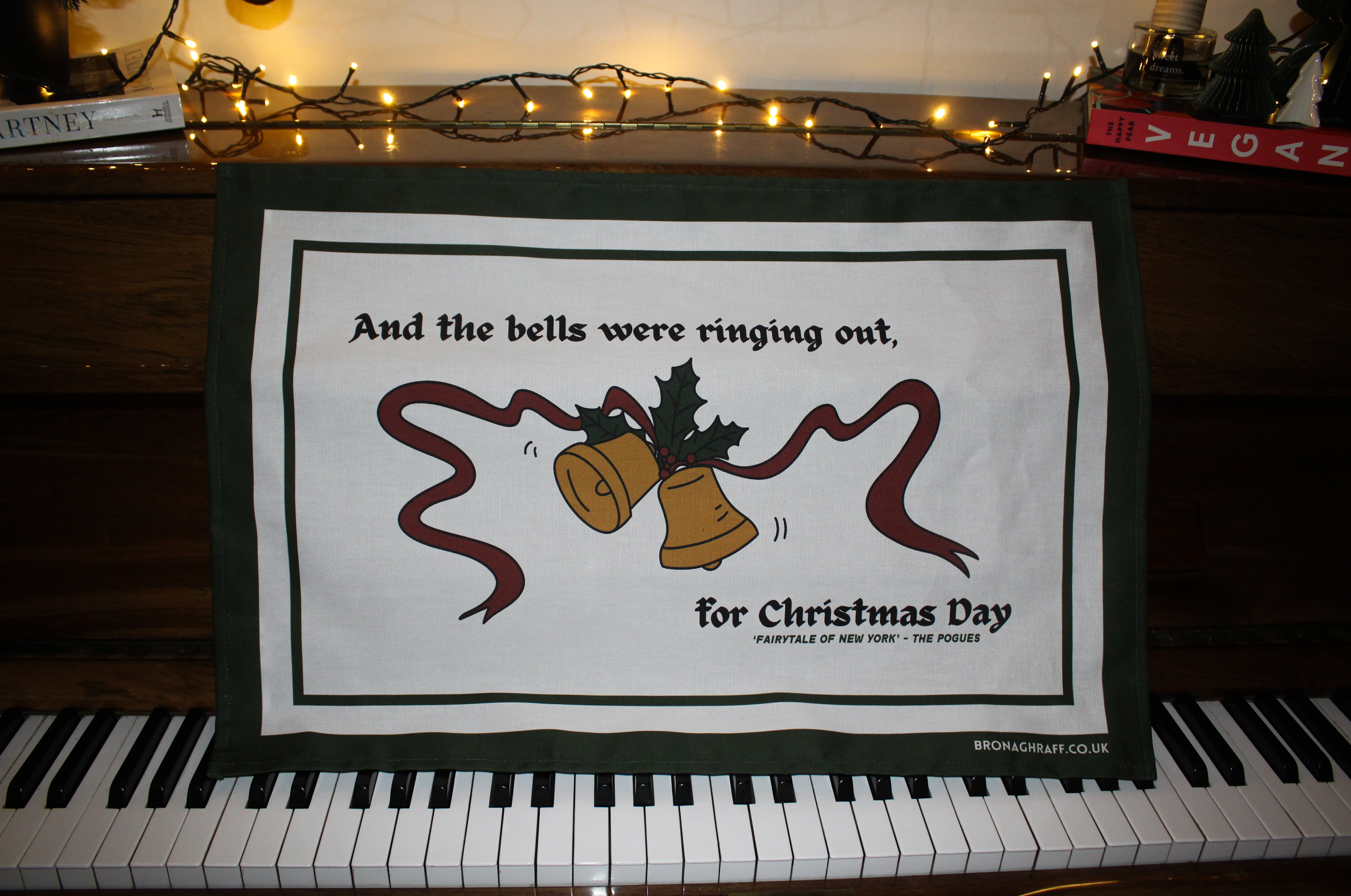 Irish Christmas tea towel with traditional festive illustrations of bells, holly, and ribbons, captioned with lyrics from a iconic Pogues song