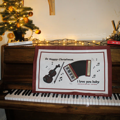 A Christmas tea towel featuring a fiddle and accordion with the lyric 'So Happy Christmas, I Love You Baby' from Fairytale of New York.