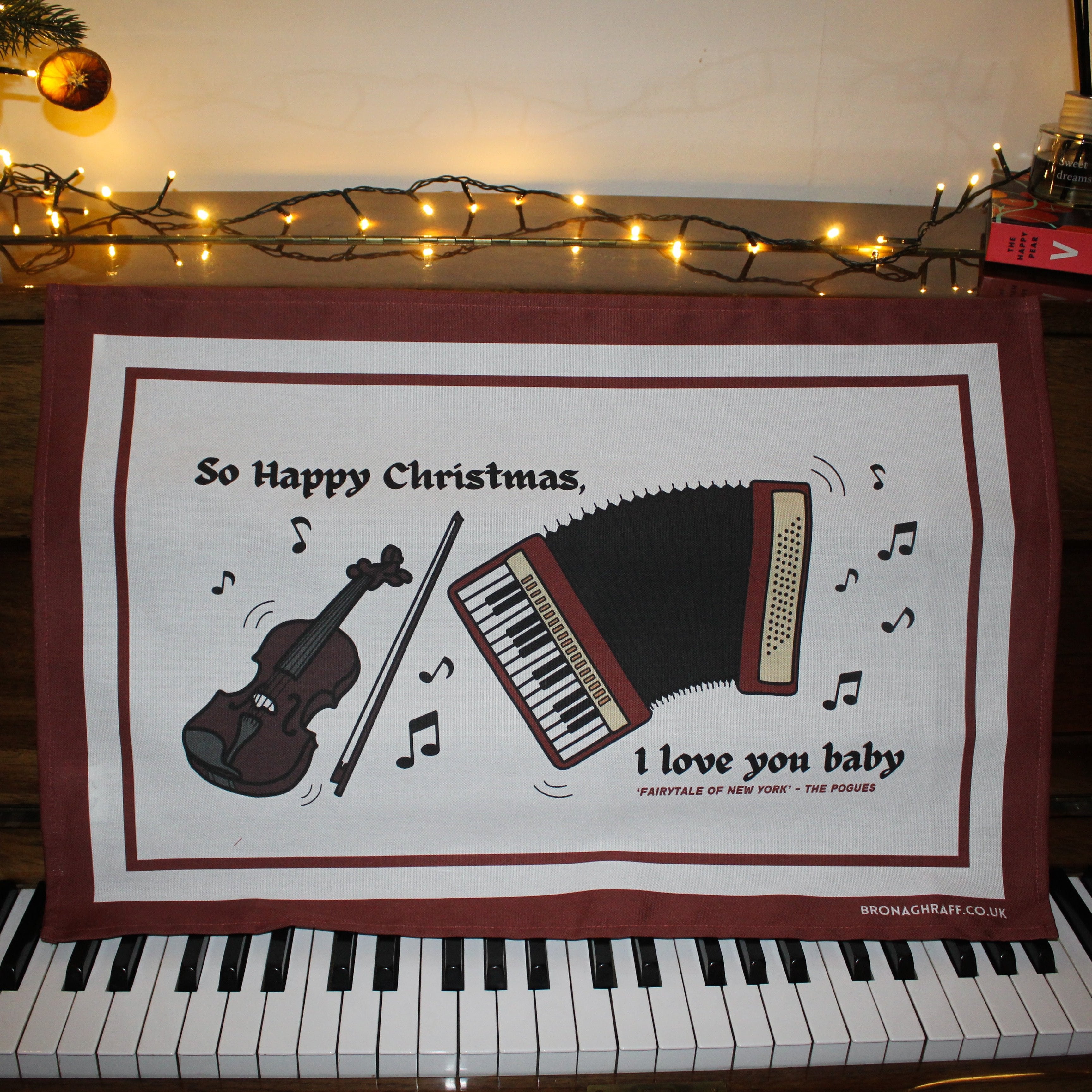 A nostalgic Irish tea towel blending music and Christmas, with a fiddle, accordion, and lyrics from a iconic Pogues song.
